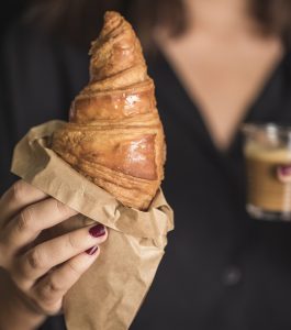 Person holding a croissant and an espresso