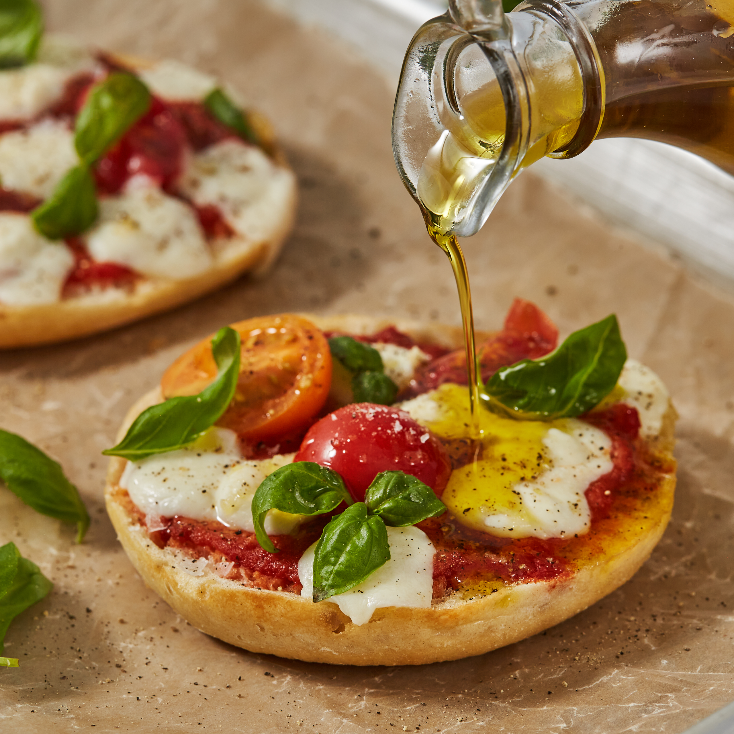 A small pizza made on a RUSTICA brand round bun. The small pizza is being drizzled with olive oil.
